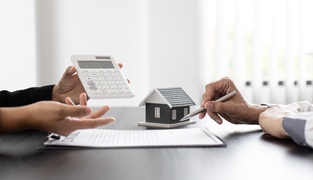 Two people discussing benefits of electrification for multifamily property management. One of thenm holding calculator, the other is taking notes. There is a house figure in the background.