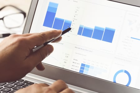 image of laptop screen with charts and someone pointing at charts with pen in hand